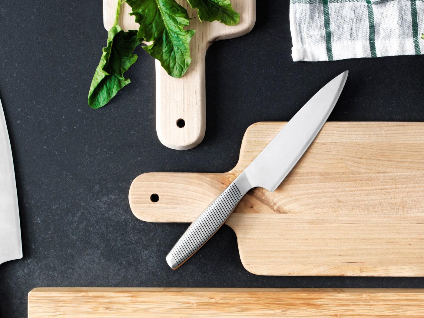 Ein IKEA 365+ Kochmesser in Edelstahl liegt auf einem Schneidebrett aus Holz, das sich neben zwei anderen Schneidebrettern aus Holz befindet.