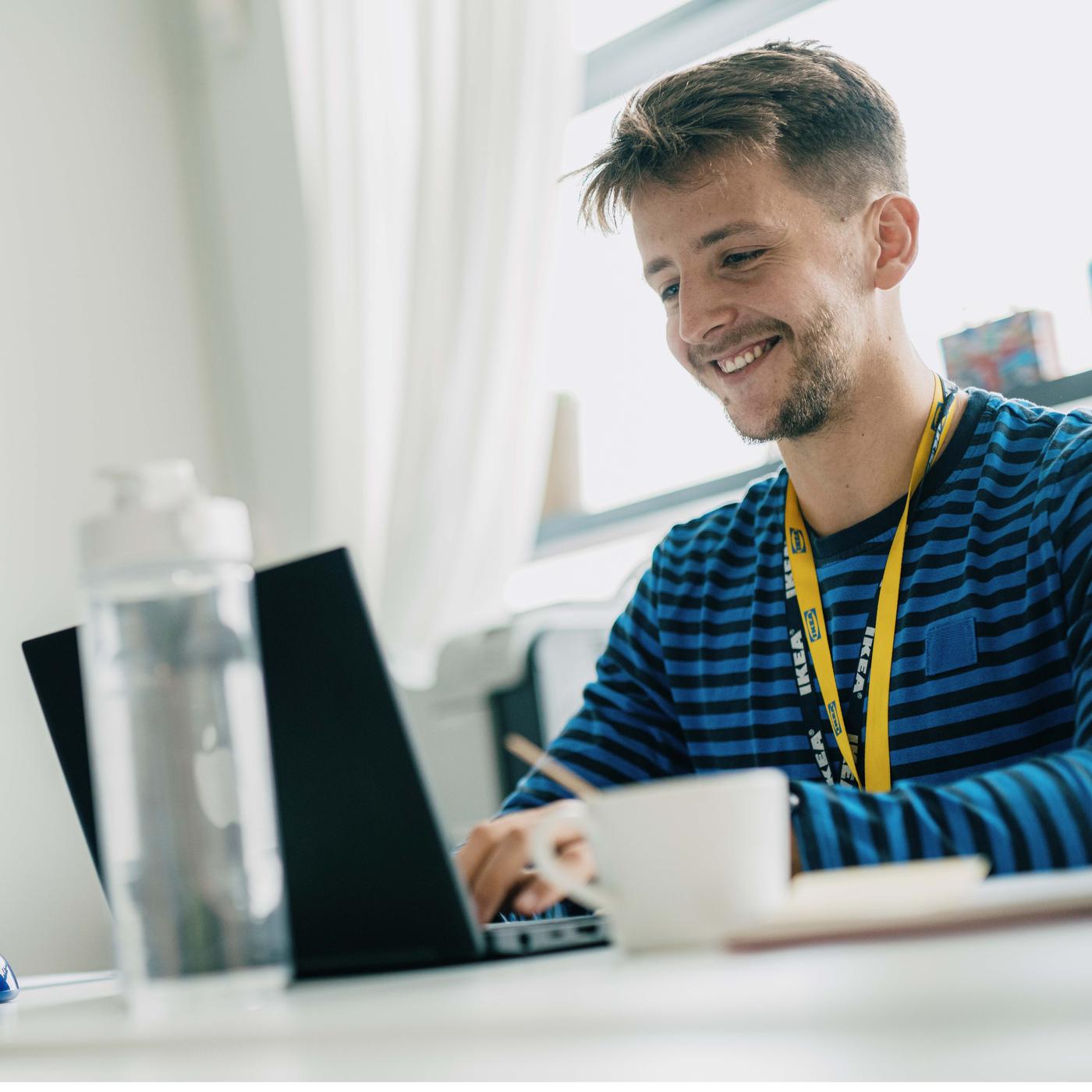 Ein IKEA Küchenplaner in blauer Uniform sitzt am Laptop und plant eine Küche. 