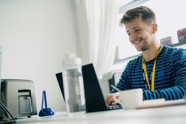 Ein IKEA Lehrling zum E-Commerce-Kaufmann sitzt am Schreibtisch vor dem Laptop und lächelt.