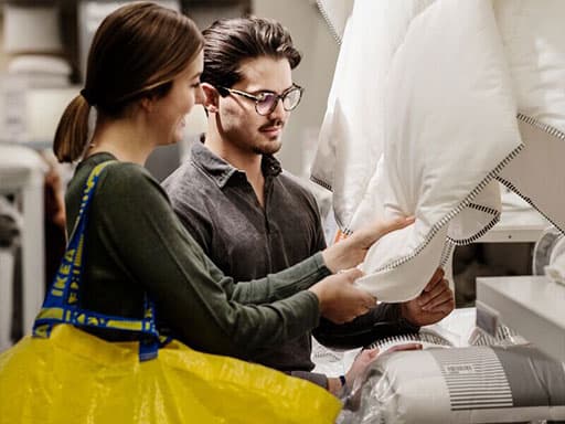 Ein junger Mann in schwarzer Kleidung geht durch ein IKEA Einrichtungshaus und trägt eine gelbe IKEA Einkaufstasche.
