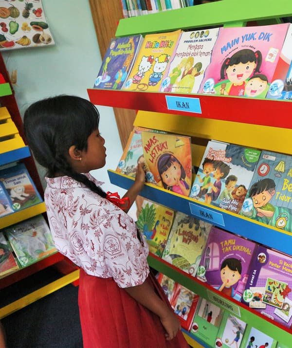 Ein Kind sucht sich in einer bunten Kinderbibliothek ein Buch aus.
