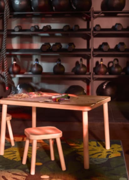 Ein Kindertisch mit Hocker vor einer Wand mit Kettlebells.