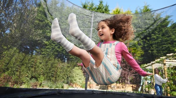 Ein kleines Mädchen springt sitzend auf einem Trampolin nach oben.