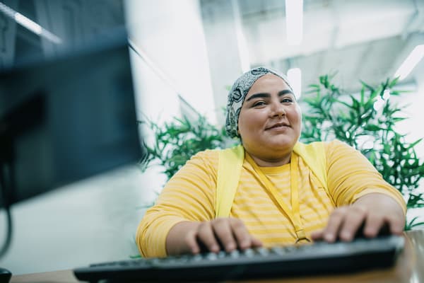 Ein lächelnder IKEA Lehrling zur E-Commerce-Kauffrau sitzt am Schreibtisch und arbeitet am PC.