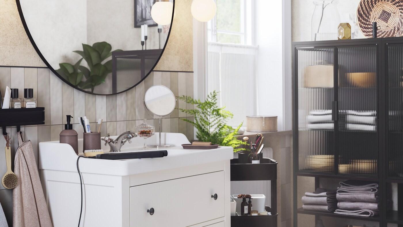 Ein LINDBYN Spiegel hängt über einem weissen HEMNES/RÄTTVIKEN Waschbeckenschrank mit zwei Schubladen. Neben dem Spiegel befindet sich eine FRIHULT Wandleuchte.