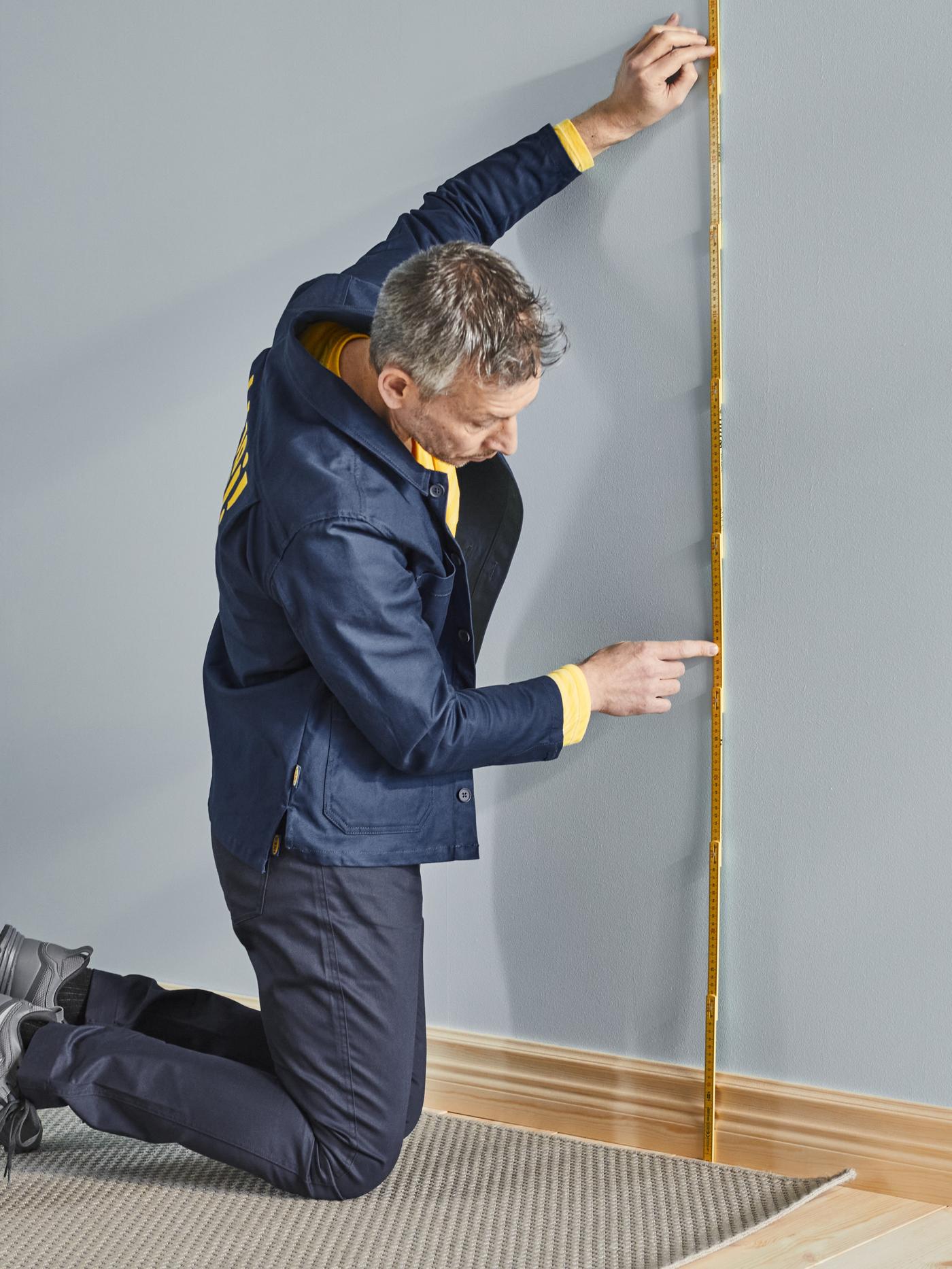 Ein Mann misst eine Wand mit Hilfe eines Zollstockes aus.