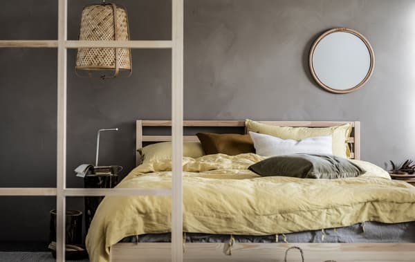 Ein minimalistisch gehaltenes Schlafzimmer in erdigen Farbtönen mit Spiegel über dem Bett.