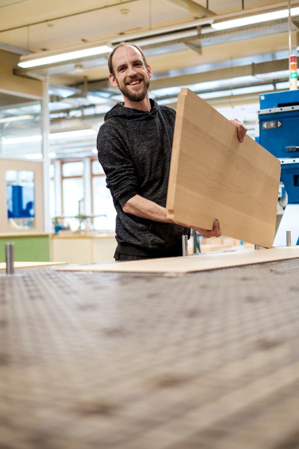 Ein Mitarbeitender des Unternehmens VEBO hält lächelnd ein zugeschnittenes Holzbrett in der Hand. 
