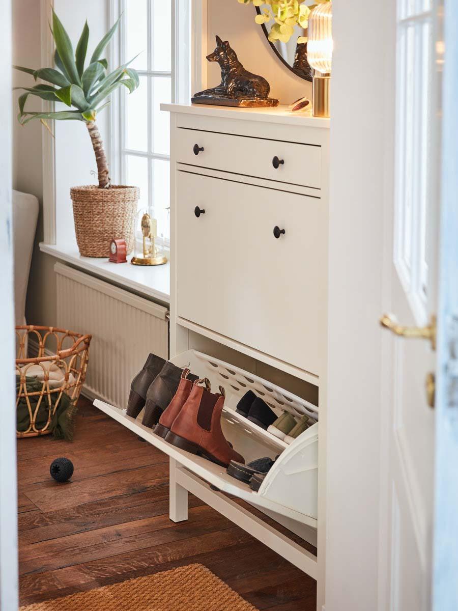 Ein schmaler weißer Schuhschrank im Landhausstil steht an einer Wand. Das untere Schuhfach mit Schuhen ist geöffnet.
