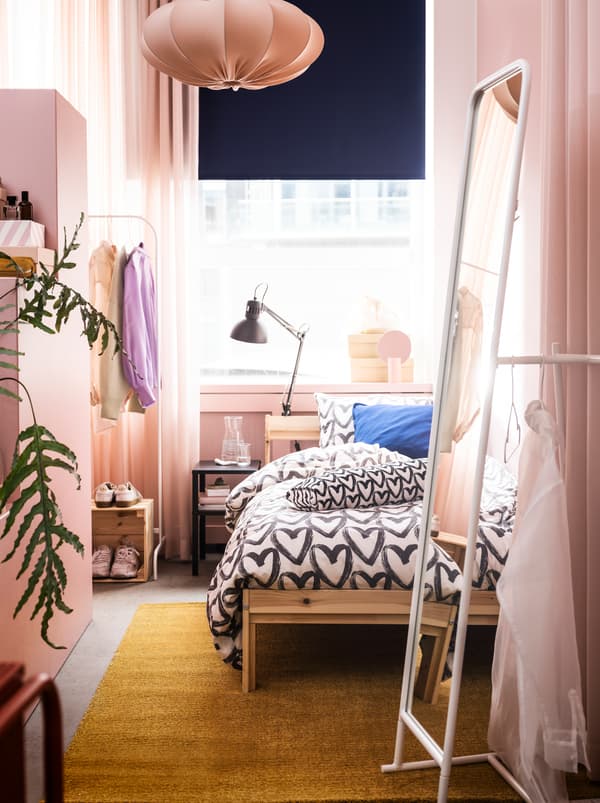 Ein schmales Zimmer mit dem NEIDEN Bettgestell, einem KNAPPER Spiegel und rosafarbenen Accessoires.