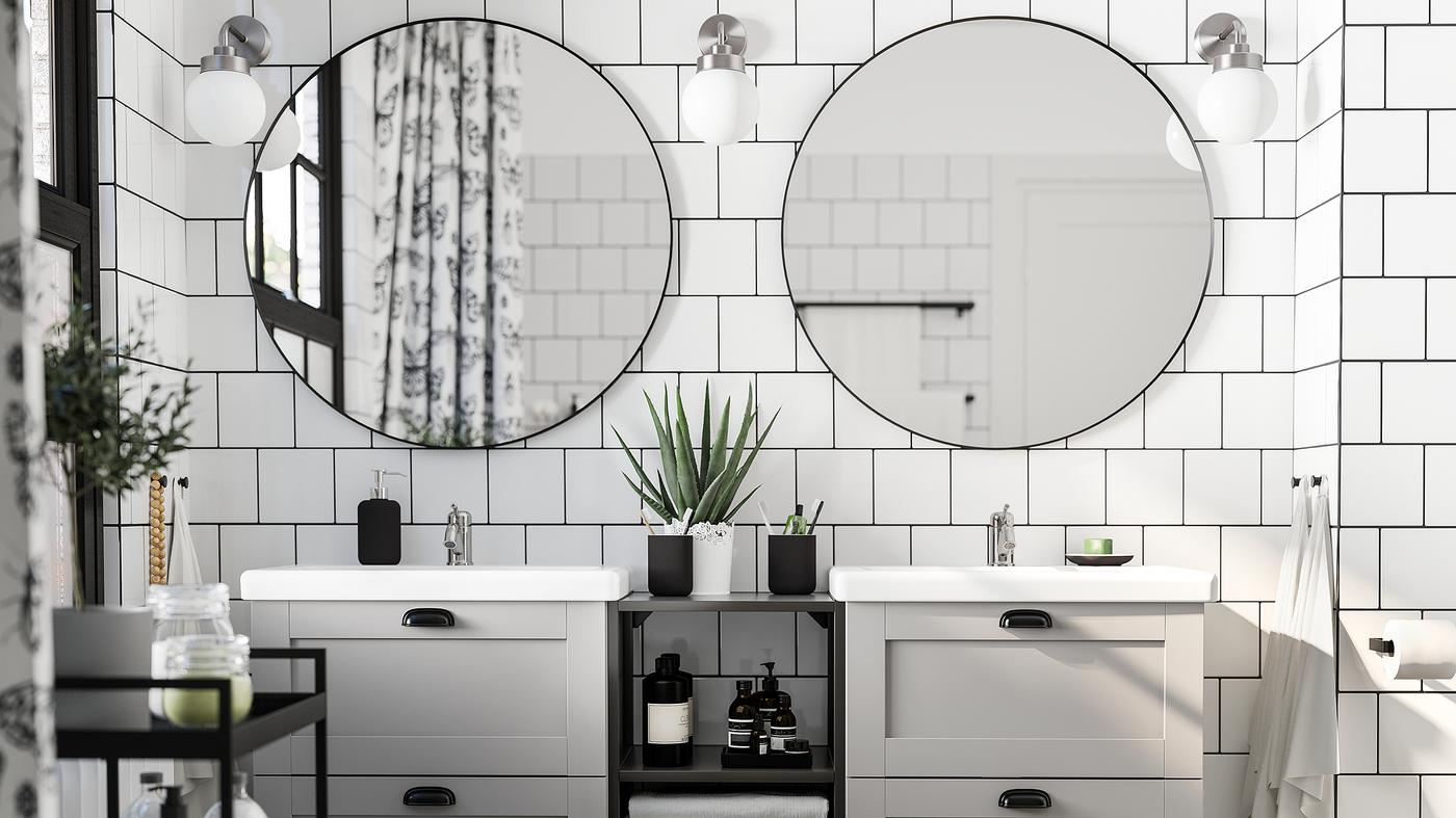 Ein Schwarz-Weiss gestaltetes Badezimmer mit zwei runden Spiegeln, weissen Waschbecken und ENHET Aufbewahrungslösungen.