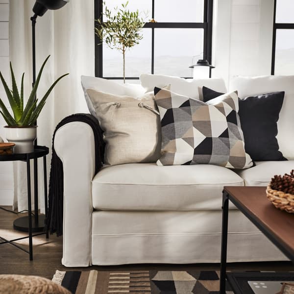 Ein Sofa mit einem grauen Plaid und dekorativen Kissen in Beige, Schwarzgrau und mit grafischem Muster. Vor dem Sofa liegt ein passender Teppich. 