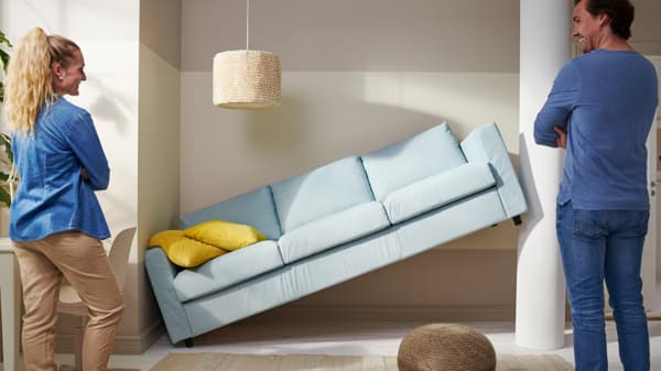 Ein Sofa steckt quer zwischen zwei Wänden ein Man und eine Frau betrachten es, lachend darüber, dass es nicht an die geplante Stelle passt.