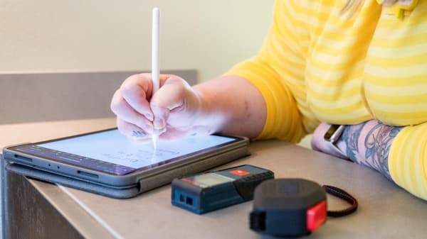 Ein Tablet, auf dem jemand mit einem Eingabestift eine Küchenplanung aufzeichnet. Daneben liegen Massband und Laser-Messgerät. 