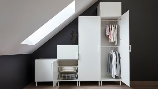 Ein weißer IKEA PLATSA Kleiderschrank steht unter einer Dachschräge. Die rechte Türe des Kleiderschrankes ist offen und man kann Kleiderstangen sehen.