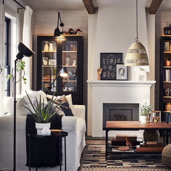 Ein Wohnzimmer mit einem weißen Sofa, Leuchten und einem Beistelltisch in Schwarz, einem beige gemusterten Teppich und zwei Couchtischen in schwarzem Metall und in Holz
