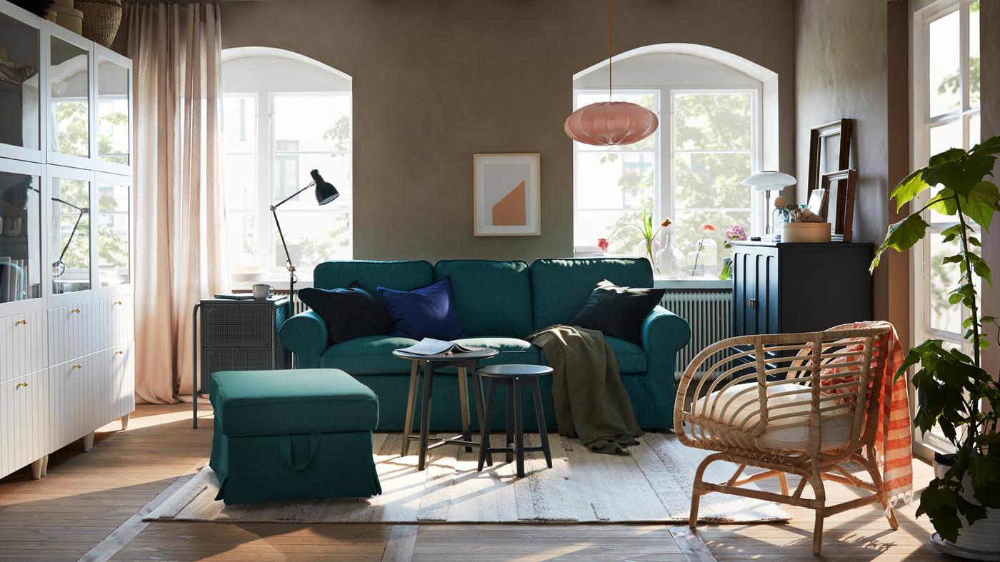 Ein Wohnzimmer mit Sofa und Hocker in tiefem Türkis, einer weissen Aufbewahrungskombination und einem blaugrünen Schrank