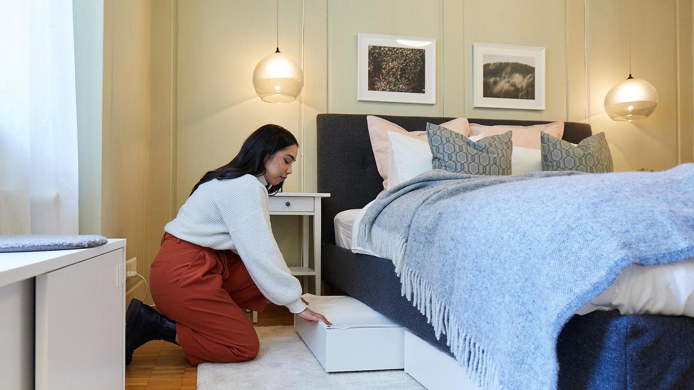 Eine Frau schiebt einen Bettkasten unter ein Bett