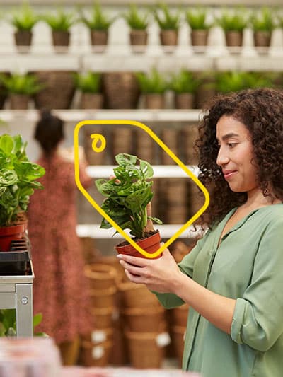 Eine Frau sieht sich eine Pflanze in der IKEA Selbstbedienungshalle an