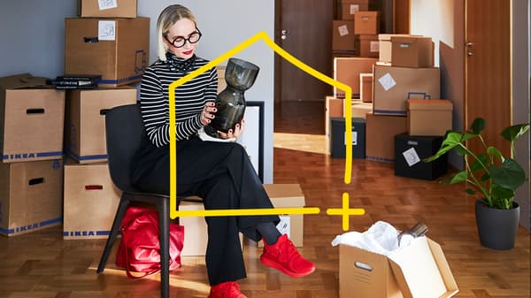 Eine Frau sitz in einem Raum voller Umzugskartons und verpackt eine Vase