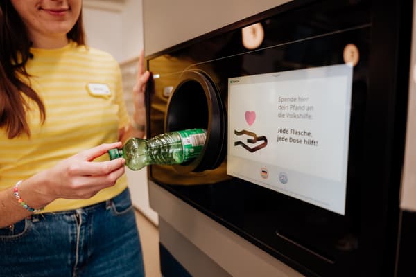 Eine Frau wirft eine Flasche in eine Recycling Maschine