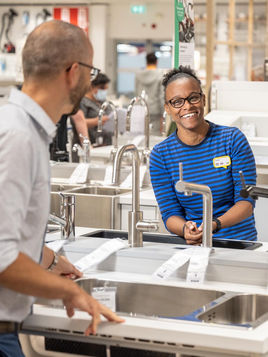Eine IKEA Küchenplanerin unterhält sich lachend mit einem Kunden und berät diesen bezüglich Einbauspülen.
