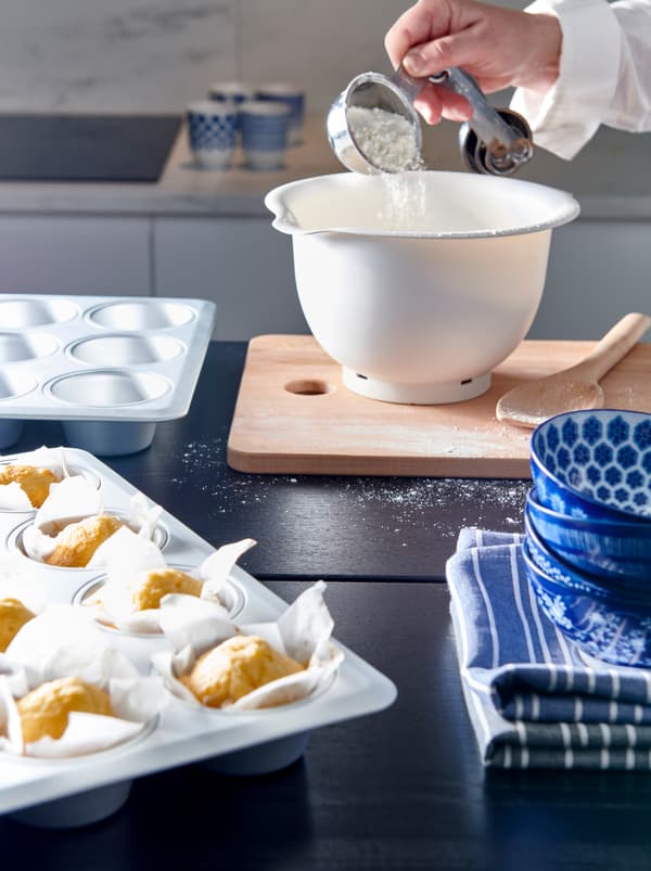 Eine Küche, in der gebacken wird. Eine Person schüttet Mehl in eine ENTUSIASM Schüssel, die neben einer Backform mit frisch gebackenen Muffins steht.