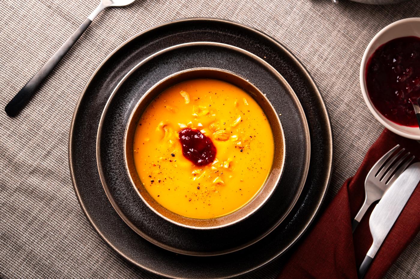 Eine Kürbissuppe, angerichtet in einer schwarzen Schale und einem schwarzen Teller.