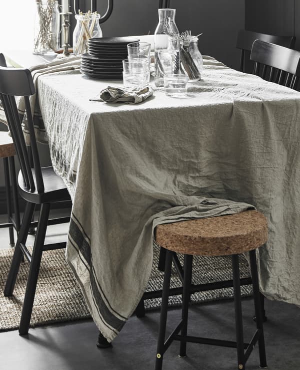 Eine Mischung verschiedener Sitzgelegenheiten an einem grossen Esstisch, u. a. mit VARDAGEN Tischdecke in Beige.
