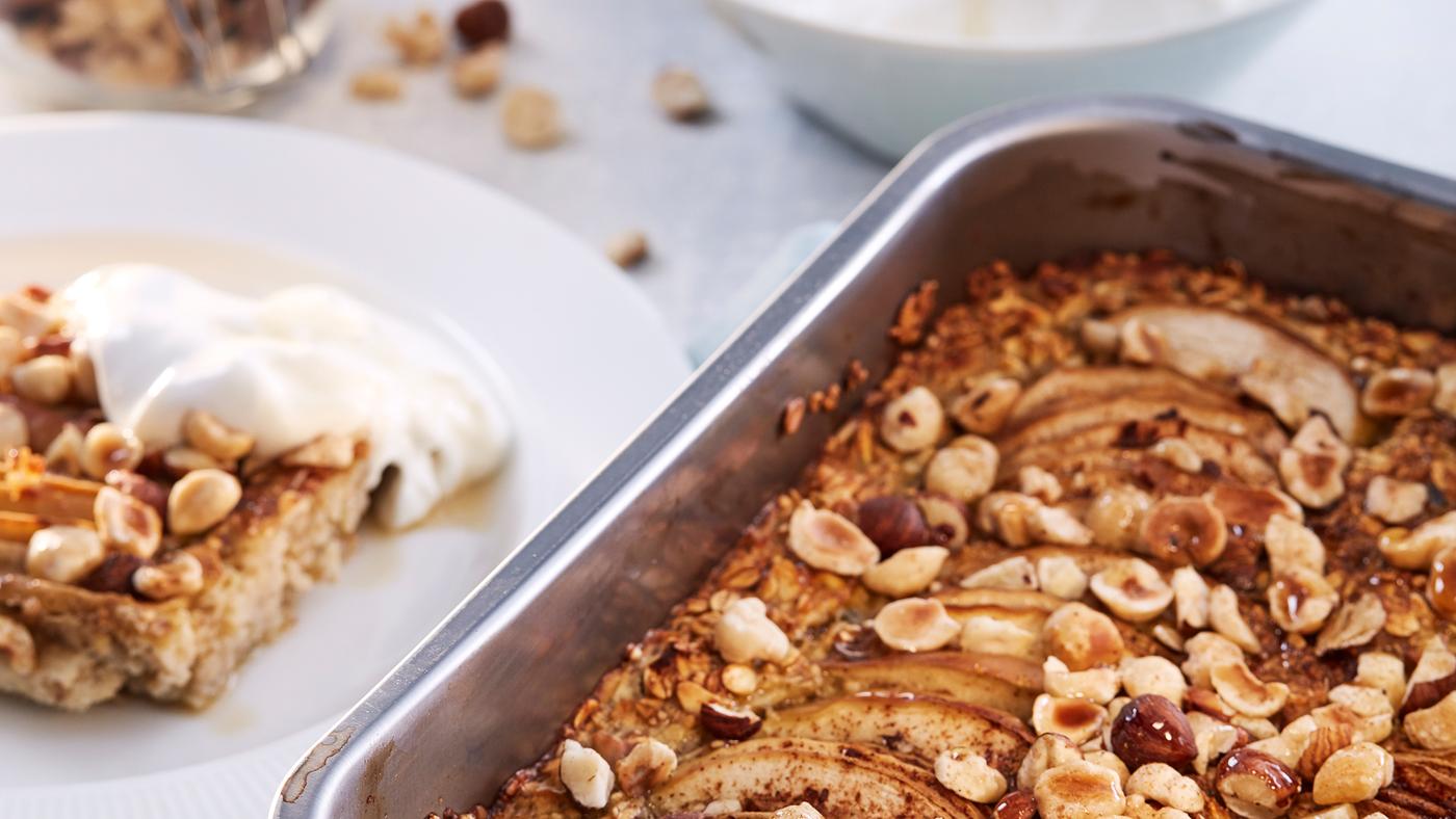 Eine Ofenform mit HJÄLTEROLL Körnermischung steht neben einem weissen Teller mit etwas Porridge und einem Klecks Joghurt darauf.