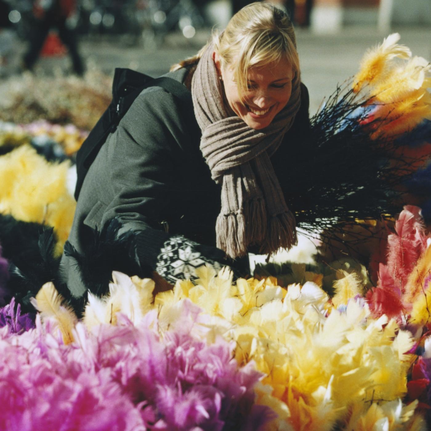 Eine Person in einer grünen Jacke kauft umgeben von bunten Frühlingsblumen Osterschmuck ein.