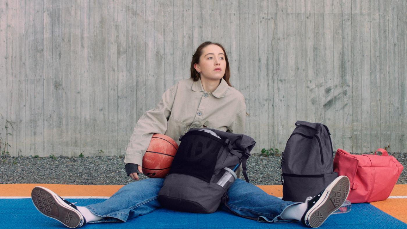 Eine Person sitzt mit einem Basketball unter dem Arm auf einem Basketballplatz, umgeben von verschiedenen IKEA Taschen.