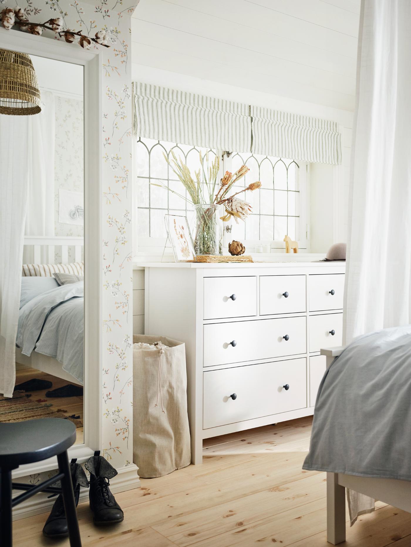 Eine weiss gebeizte HEMNES Kommode mit 8 Schubladen und ein weiss gebeiztes HEMNES Bettgestell stehen in einem hellen Schlafzimmer mit Holzfussboden.