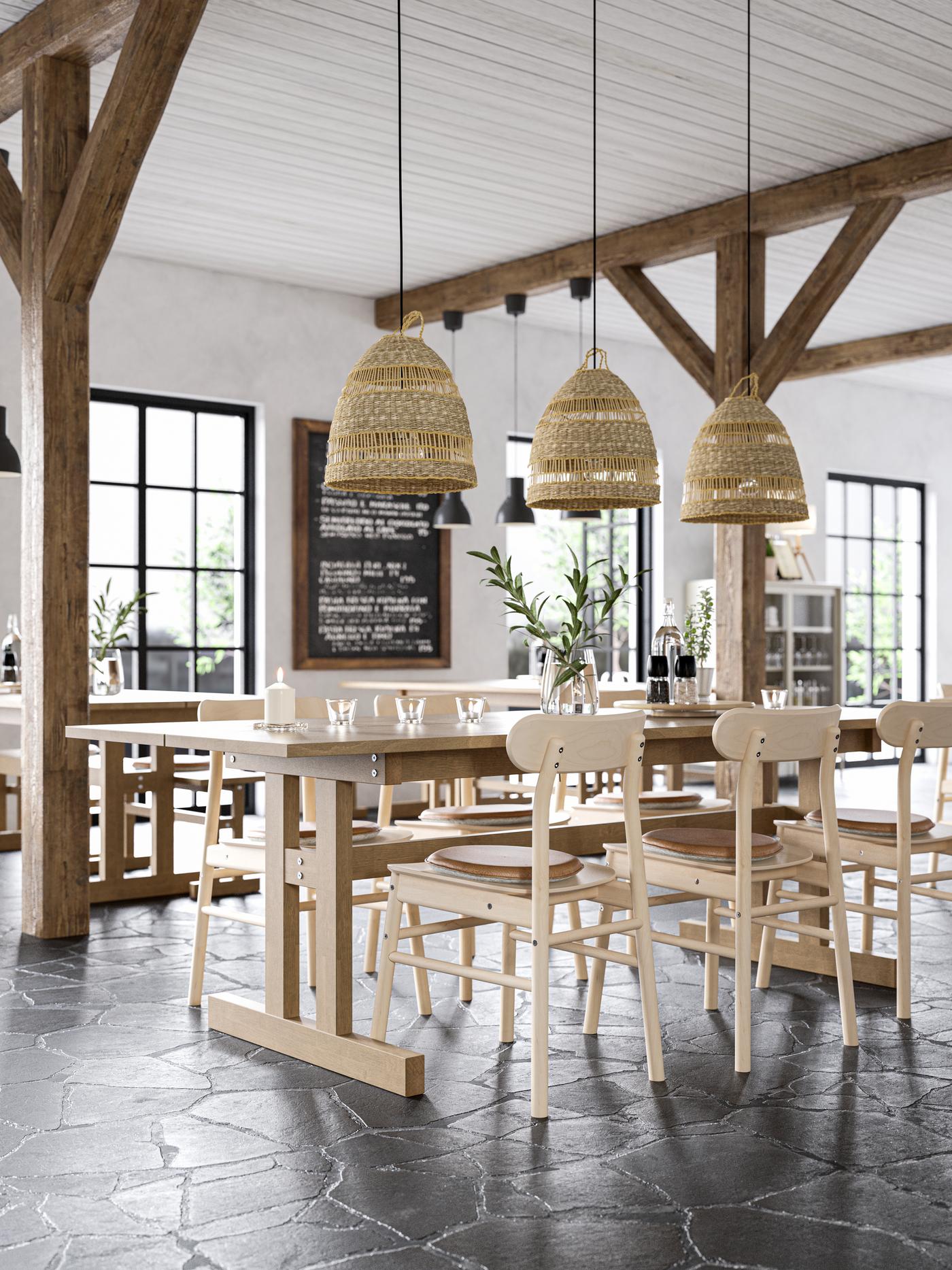 El interior de un café con grandes vigas de madera en el techo y lámparas colgantes de mimbre. También hay mesas y silas altas de madera IKEA.