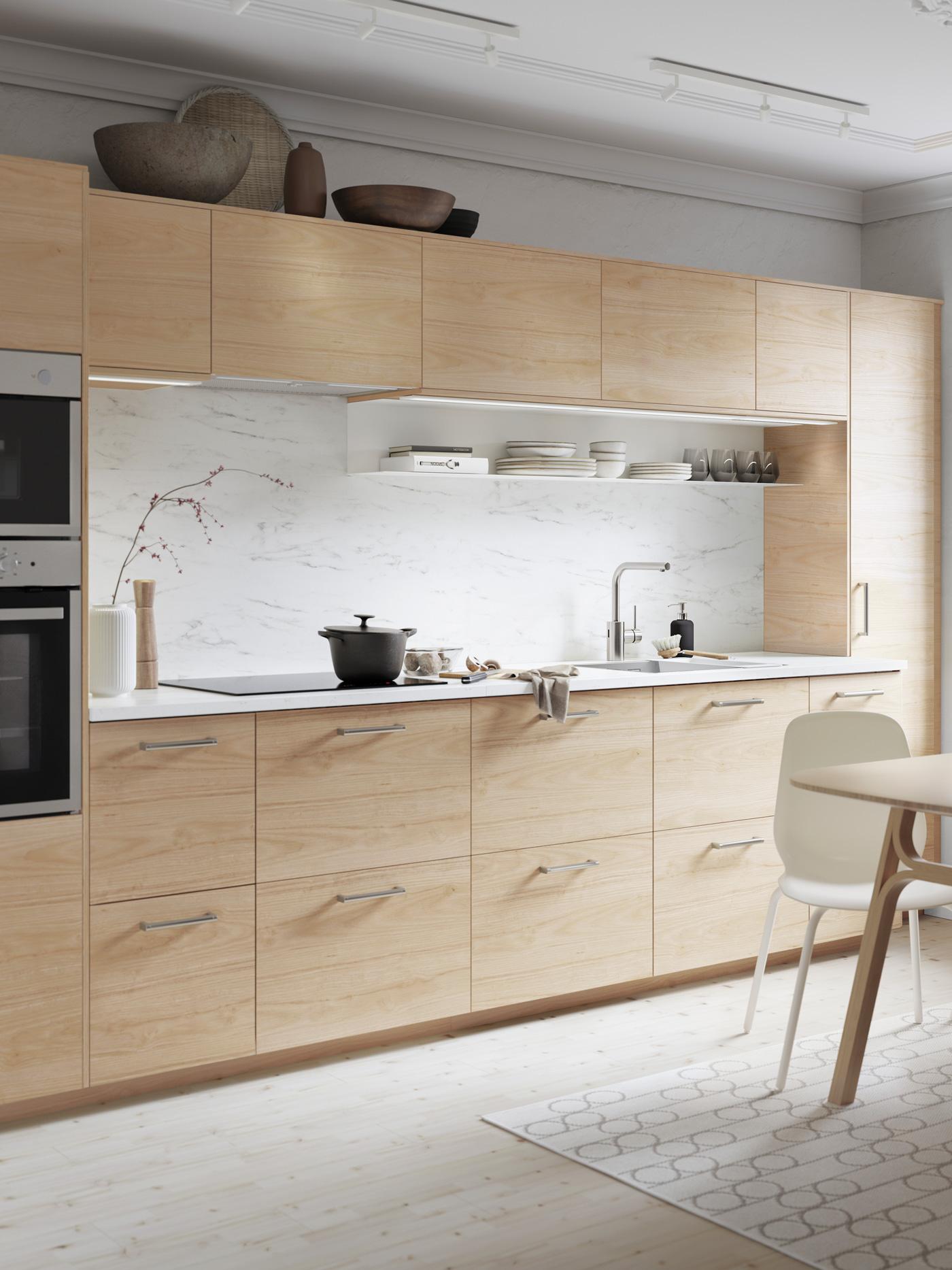 Elegante cucina nera con illuminazione sottopensile sotto ai mobili superiori. Due portavasi neri con piante sopra al piano di lavoro - IKEA