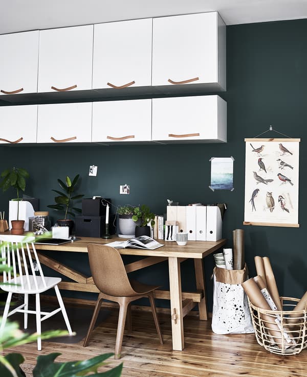 Éléments blancs et table en bois sur fond de mur vert foncé.