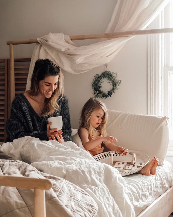 Emilie and her daughter Brook sitting in a GJÖRA birch bed with rumpled white linens.