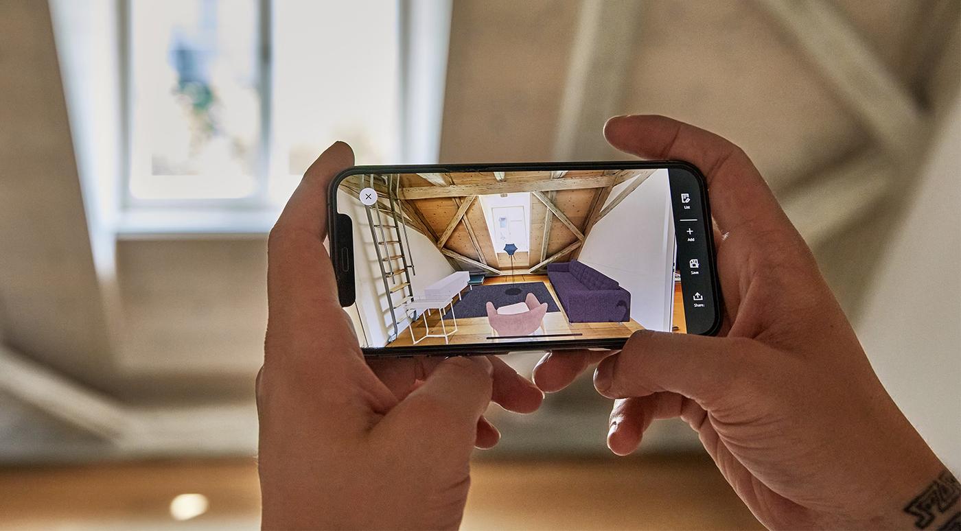 En bild på en person som använder sin telefon och appen IKEA Kreativ för att skanna sitt rum och digitalt placera produkter där.