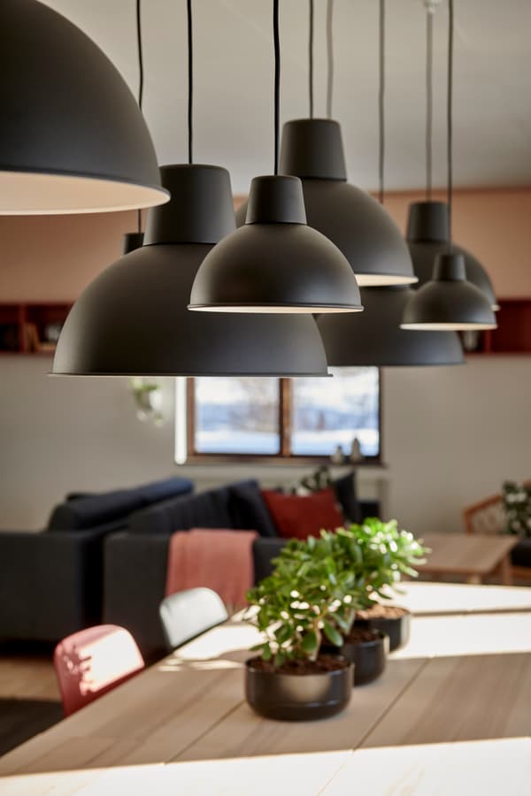 En detaljbild på svarta taklampor som hänger över ett långt matbord. 