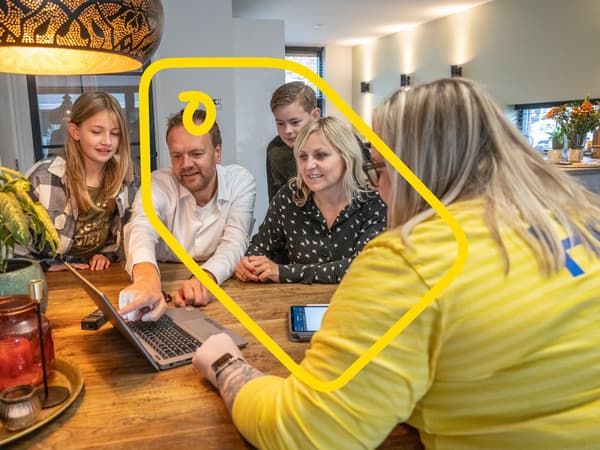 En IKEA‑medarbetare går igenom köksplanen vid ett stort träbord hemma hos en kundfamilj.