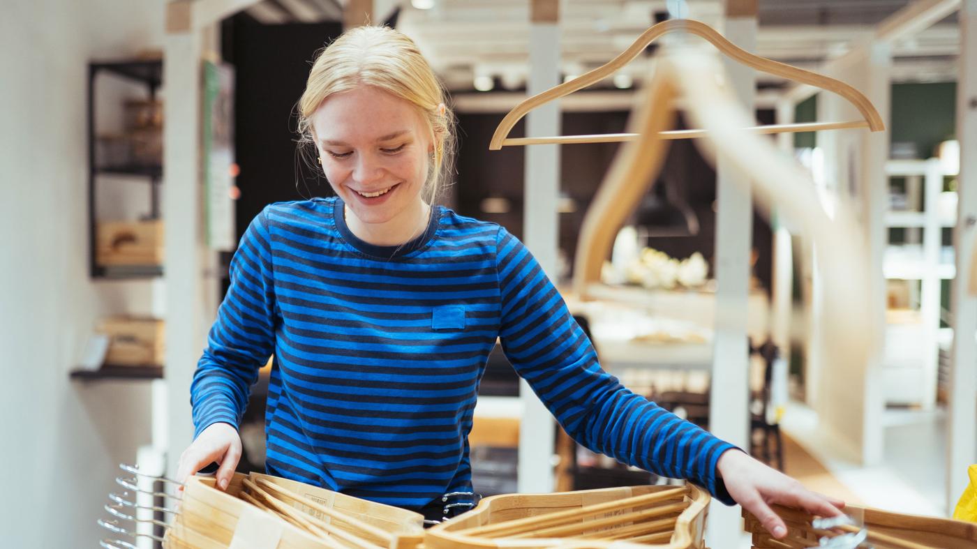 En kvinde holder en bøjle og ser på tøj med et eftertænksomt udtryk i ansigtet.