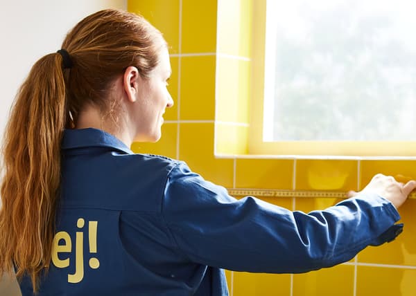 En kvinde i ikea-uniform måler op på et gult badeværelse.