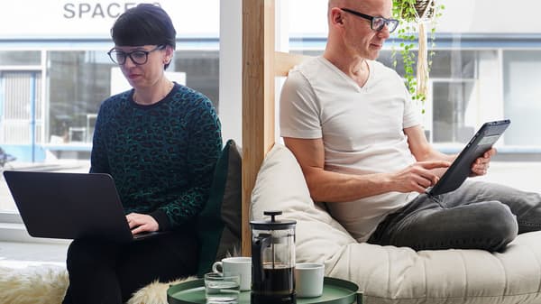 En kvinna med en laptop i knäet sitter bredvid en man som håller i en touchskärm.