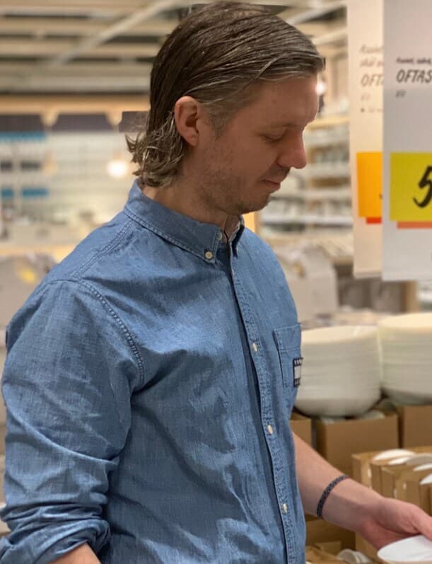 En person i blå skjorta står i ett IKEA varuhus och håller i en tallrik.