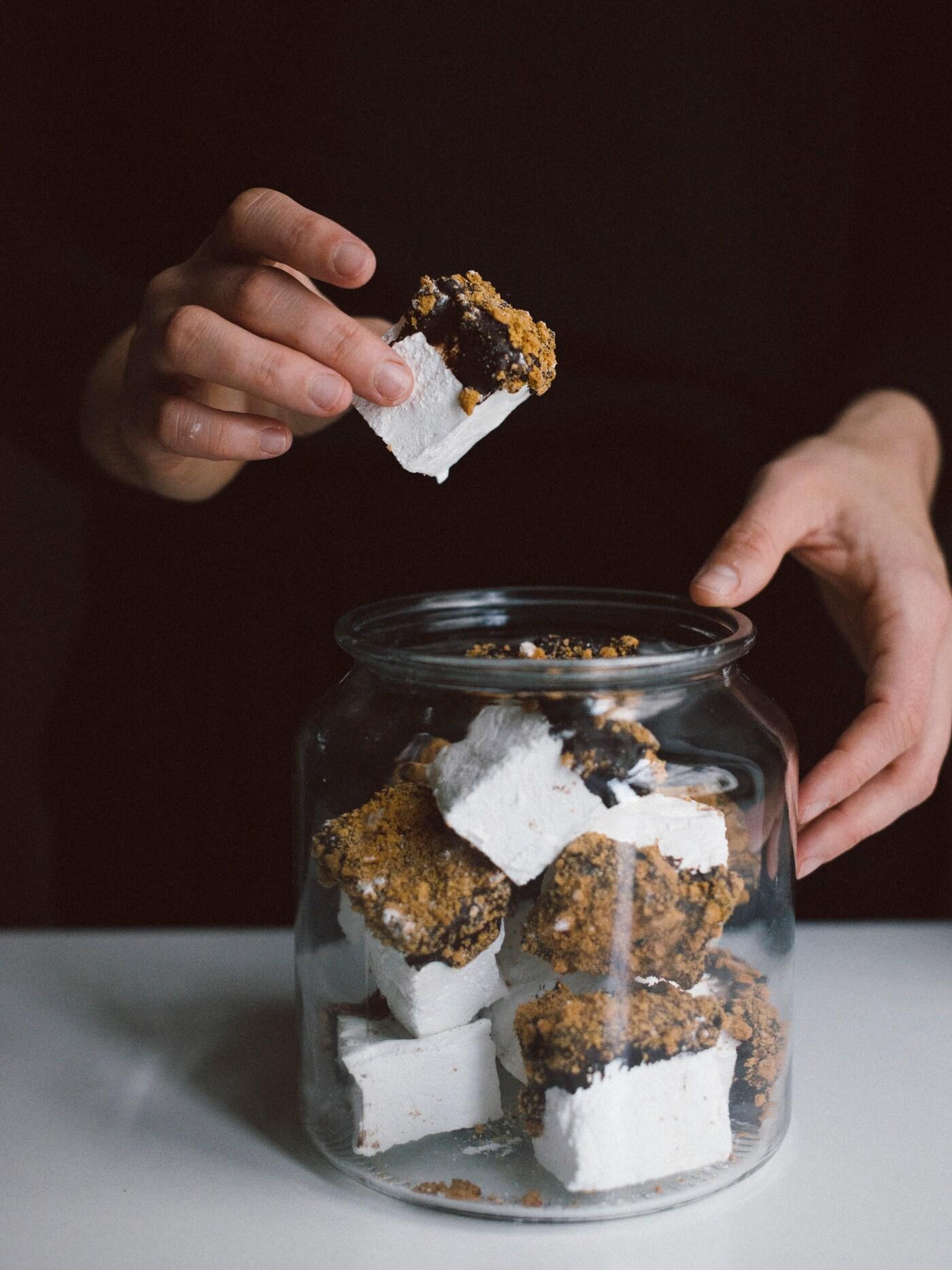 En person plockar upp en dekorerad marshmallow ur en glasskål.