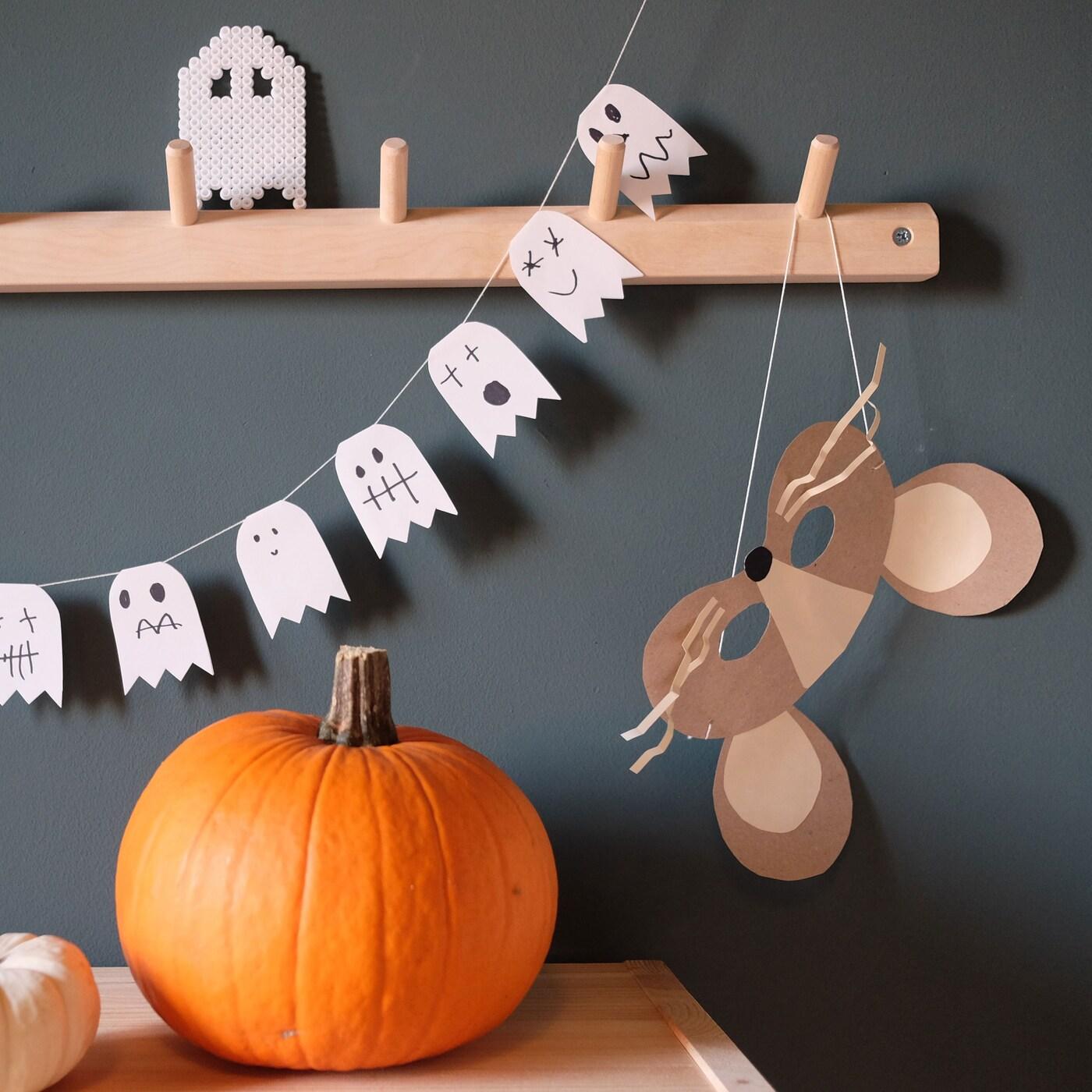 En pumpa och halloweenpyssel gjorda av papper. Vita spöken gjorda av papper hänger i en girlang.