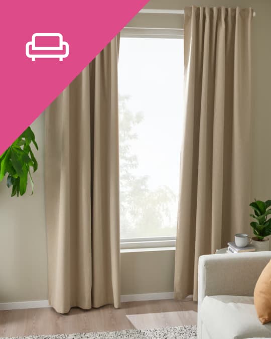 En una sala al costado de un sofá unas cortinas de tela beige cubren la mitad de un ventanal.