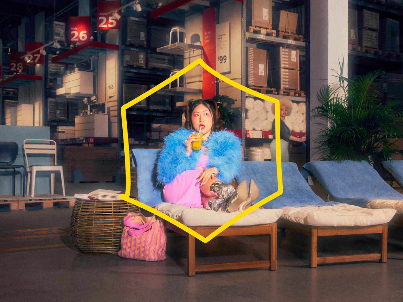 En una tienda IKEA, una mujer vestida con ropa colorida está comiéndose una piruleta en una reposera. 