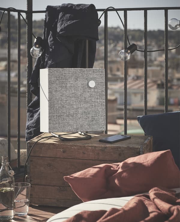 Enceinte grise posée sur une caisse sur un balcon, avec des lumières et des plaids.
