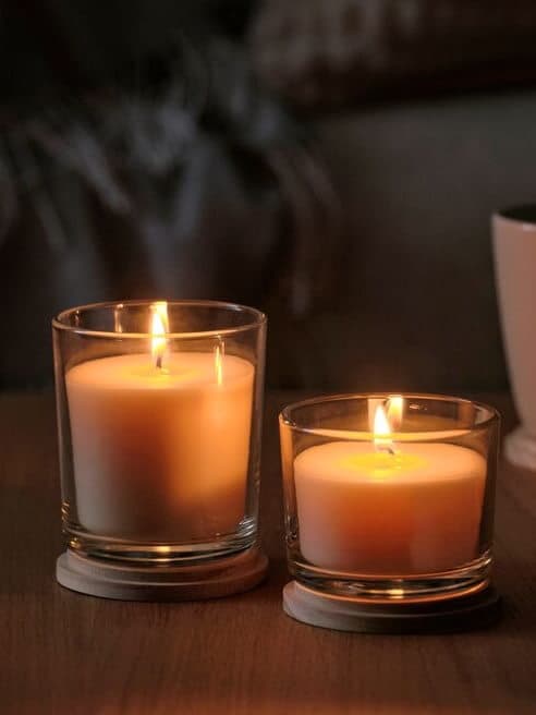 Enciende velas en una mesa de centro junto a unas flores para crear un ambiente de sala cálido y acogedor.